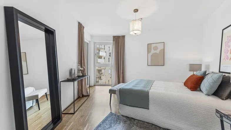 Helles Schlafzimmer mit Holzboden, großem Spiegel und Zugang zu einem Balkon.