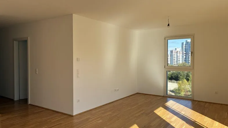 Helles Zimmer mit Parkettboden und Blick auf die Stadt durch ein großes Fenster.