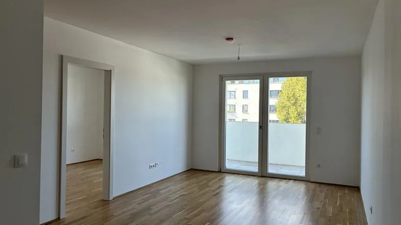 Helles Zimmer mit Parkettboden und Zugang zu einem Balkon, ideal als Wohn- oder Schlafbereich.