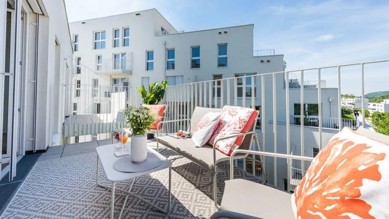 Möblierter Balkon mit modernen Sitzgelegenheiten und Blick auf die umliegenden Gebäude und die Stadt.