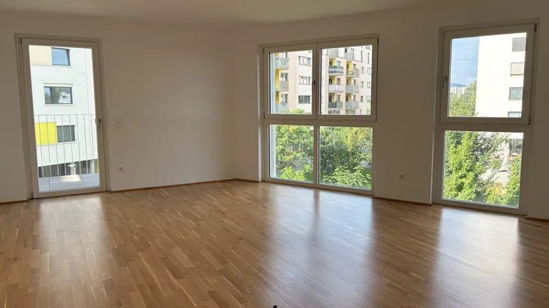 Helles Wohnzimmer mit Parkettboden, großen Fenstern und Zugang zu einem kleinen Balkon.