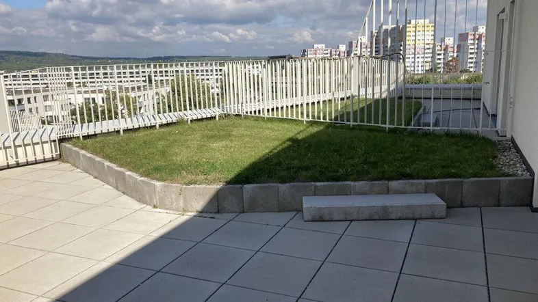 Dachterrasse mit gepflastertem Bereich, Rasenfläche und Blick auf die Stadt.