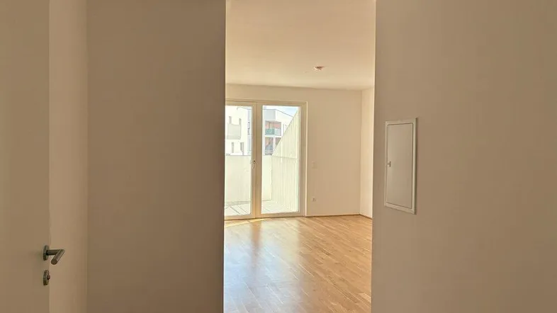Heller Flur mit Parkettboden, der in einen lichtdurchfluteten Wohnbereich mit Balkonzugang führt.