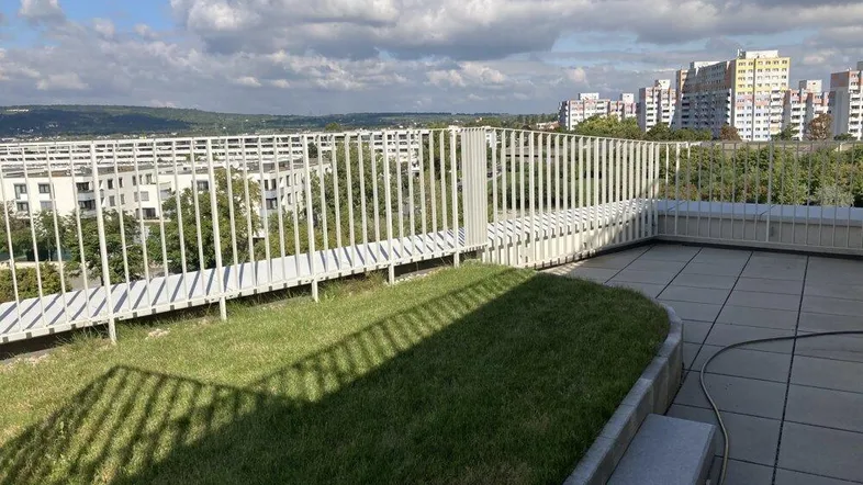 Große Dachterrasse mit Grünfläche, Fliesenboden und weitem Blick über die Stadtlandschaft.