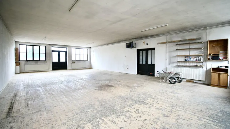 Großer, leerer Gewerberaum mit abgenutztem Holzboden, hohen Decken und mehreren Fenstern, bereit zur Renovierung.