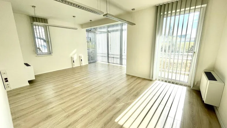 Heller Büroraum mit großen Fenstern, vertikalen Jalousien und modernem Laminatboden.