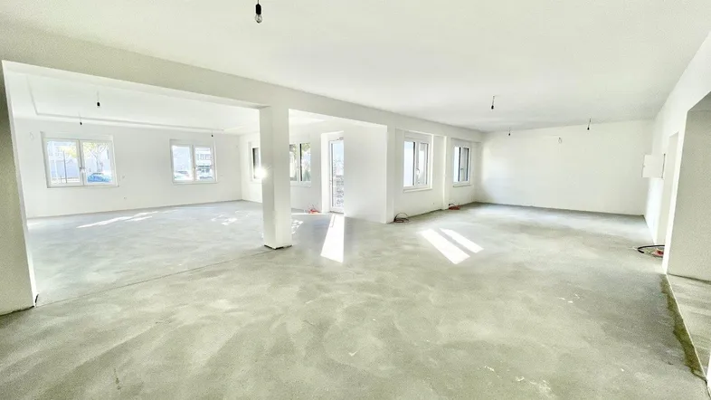 Großer, heller Gewerberaum im Rohbauzustand mit vielen Fenstern und Betonboden.