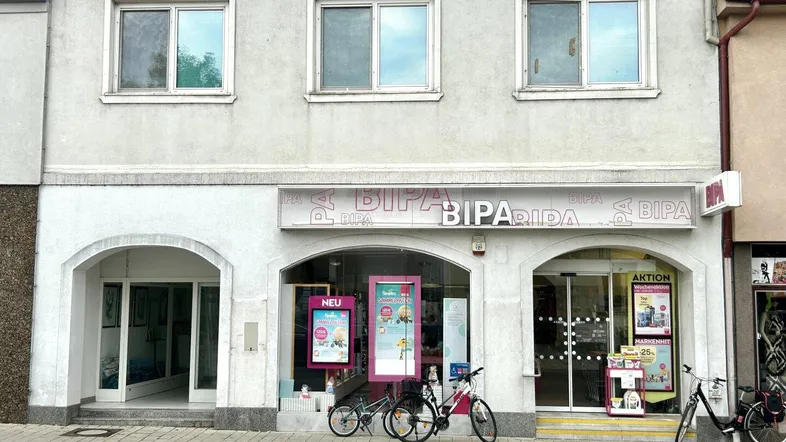 Fassade eines Gebäudes mit Geschäftsräumen im Erdgeschoss und Wohnungen darüber, Fahrräder davor.