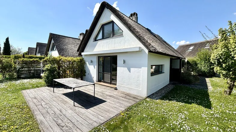 Charmantes Haus mit Reetdach, Holzterrasse und weitläufigem Garten mit Blick auf die Umgebung.