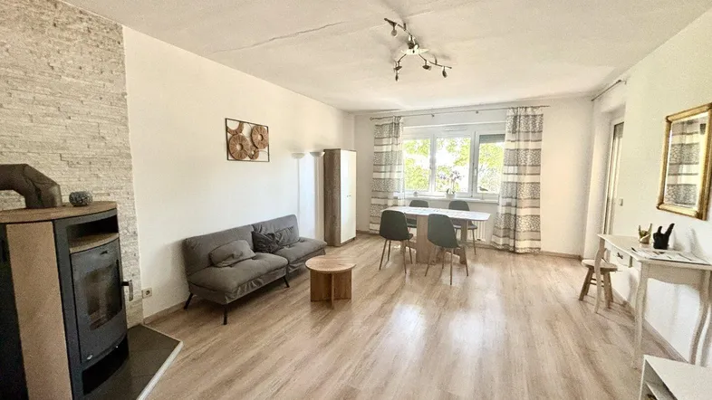 Heller Wohn- und Essbereich mit modernem Laminatboden, Kaminofen und Zugang zum Balkon.