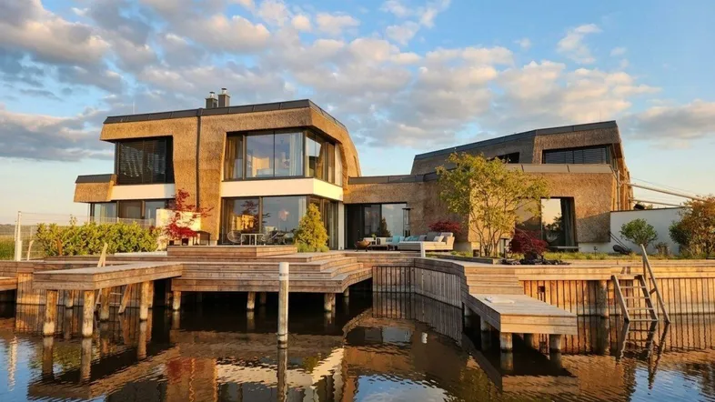 Modernes Haus mit Reetdach und Holzstegen direkt am Wasser, umgeben von Natur.