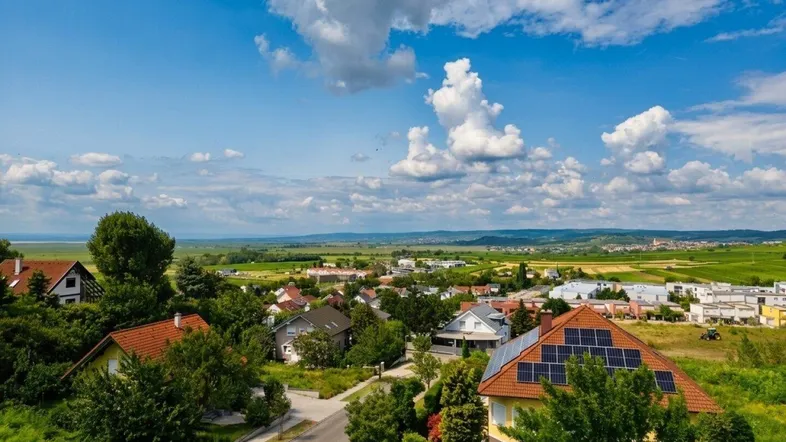 Luftaufnahme einer Wohnsiedlung mit Häusern, grünen Feldern und einem weiten Blick in die Landschaft.