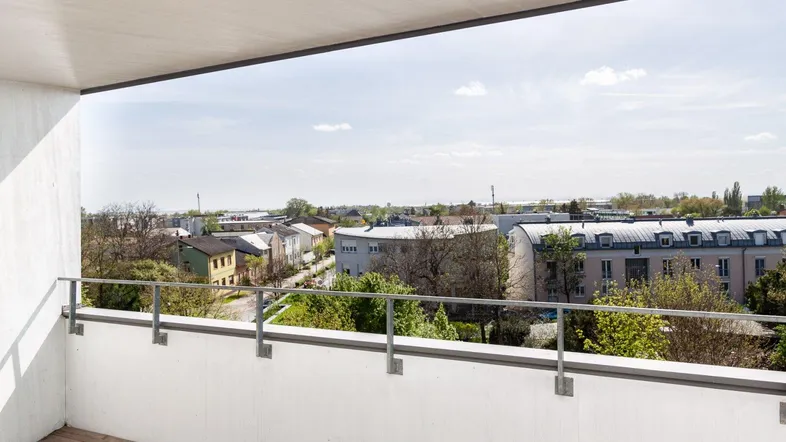 Geräumiger Balkon mit Holzboden und weitem Blick über die Stadt und grüne Umgebung.