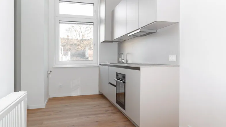 Moderne Einbauküche mit hellen Schränken, integriertem Backofen und Fenster.