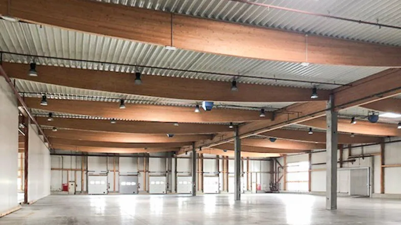 Große, leere Lagerhalle mit hohen Decken, Holzbalken und Betonboden, bereit zur Nutzung.