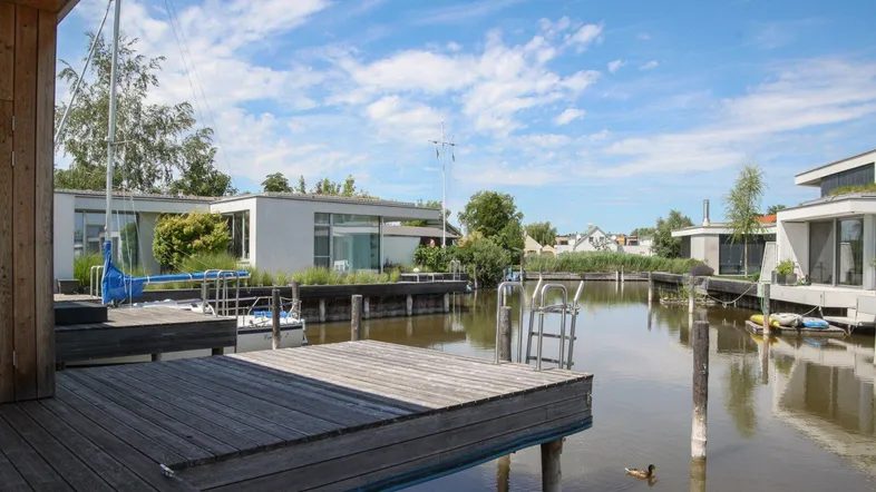 Moderne Häuser am Wasser mit privaten Bootsanlegestellen unter blauem Himmel.