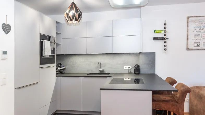 Moderne Küche mit weißen Schränken, dunkler Arbeitsplatte und integrierten Geräten, offen zum Wohnbereich.