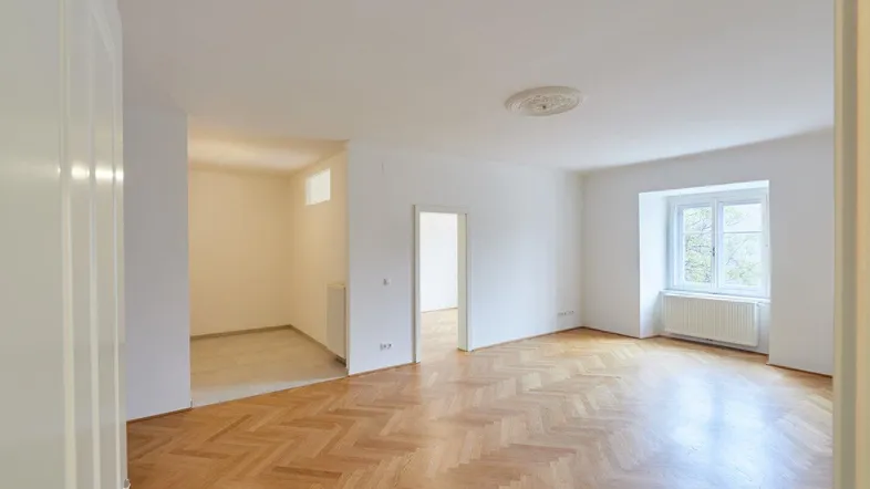 Helles Wohnzimmer mit Fischgrätparkettboden und Stuckelement an der Decke, bereit zum Einzug.