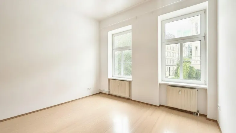Helles, leeres Zimmer mit Laminatboden und zwei Fenstern, die viel Tageslicht hereinlassen.