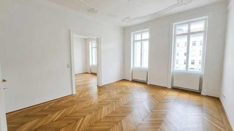 Helles Wohnzimmer mit Fischgrätparkett, hohen Decken und dekorativen Stuckelementen.