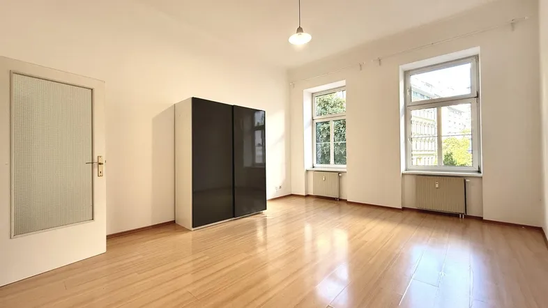 Helles, leeres Zimmer mit Laminatboden und zwei Fenstern, bereit zur individuellen Gestaltung.
