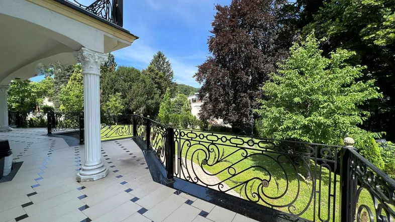 Elegante Terrasse mit kunstvollem Geländer und Blick auf den gepflegten Garten und die grüne Umgebung.