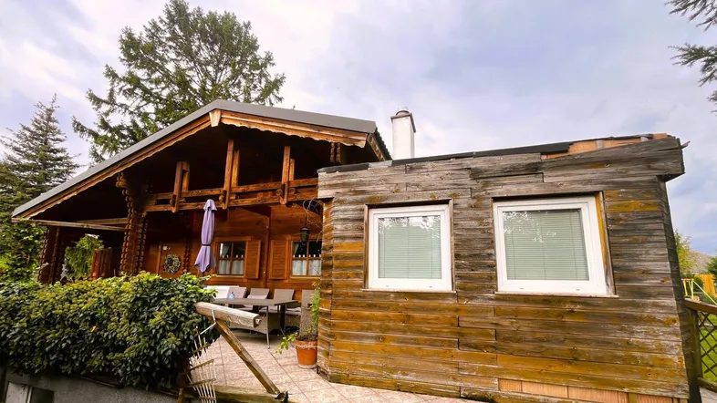 Rustikales Holzhaus mit einer gemütlichen Terrasse, umgeben von grünen Pflanzen und Bäumen.