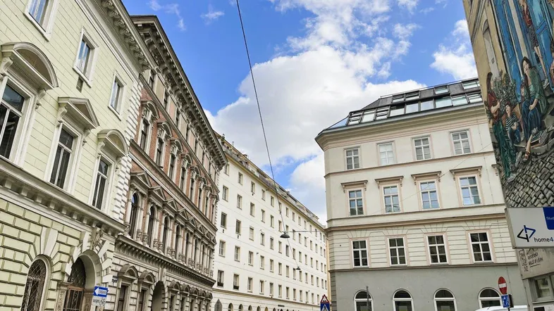 Historische Gebäude entlang einer belebten Straße unter blauem Himmel mit Wolken.