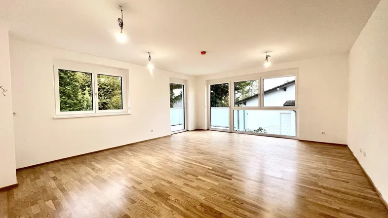 Helles, geräumiges Zimmer mit Parkettboden und Zugang zu einem Balkon, ideal als Wohn-Essbereich.