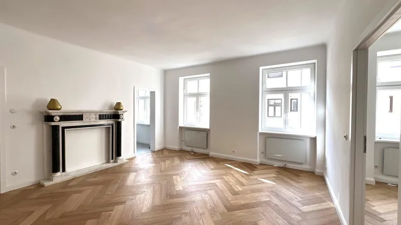 Helles Wohnzimmer mit Fischgrätparkett, dekorativem Kamin und großen Fenstern.