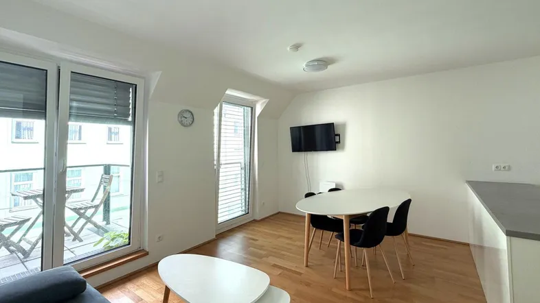 Heller Wohn- und Essbereich mit Holzboden, modernem Mobiliar und Zugang zu einem kleinen Balkon.