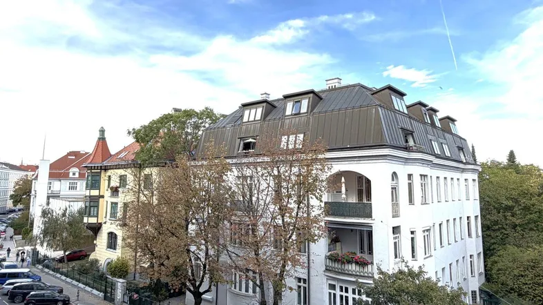 Elegantes Mehrfamilienhaus mit klassischer Architektur und Mansarddach in städtischer Umgebung.
