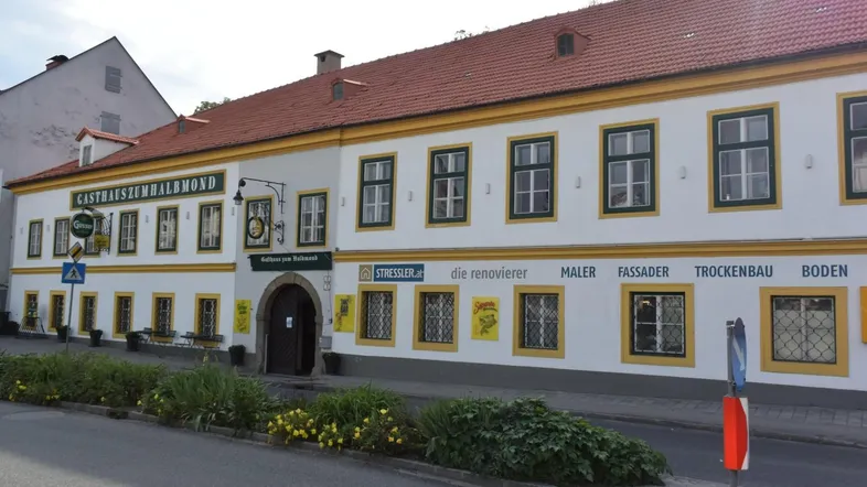 Historisches Gasthaus zum Halbmond mit traditioneller Fassade, roten Ziegeln und gelben Fensterrahmen an einer Straße gelegen.