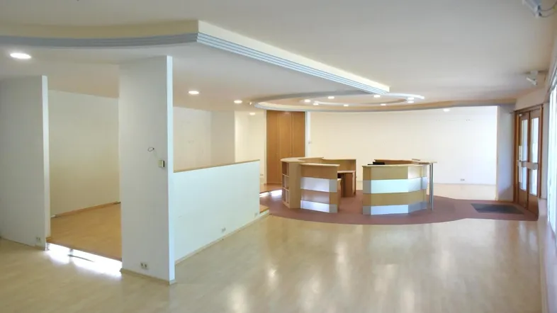 Geräumiger Bürobereich mit hellem Laminatboden, modernen Deckenelementen und viel Tageslicht durch große Fenster.