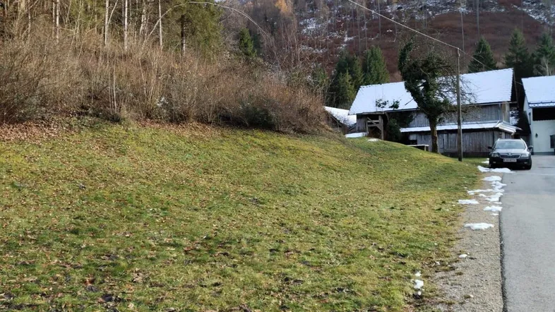 Ländliche Szene mit grasbewachsenem Hang, Holzhäusern und einem geparkten Auto am Wegrand.