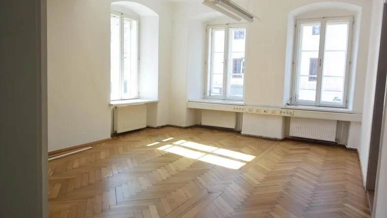 Heller Raum mit Fischgrätparkett, drei großen Fenstern und viel Tageslicht, ideal für Wohn- oder Bürozwecke.