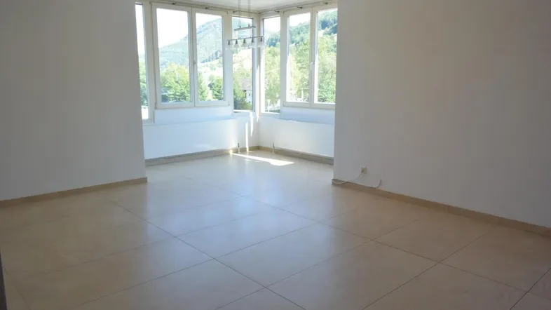Helles, leeres Zimmer mit großen Fenstern und Blick auf die Berge und grüne Landschaft.