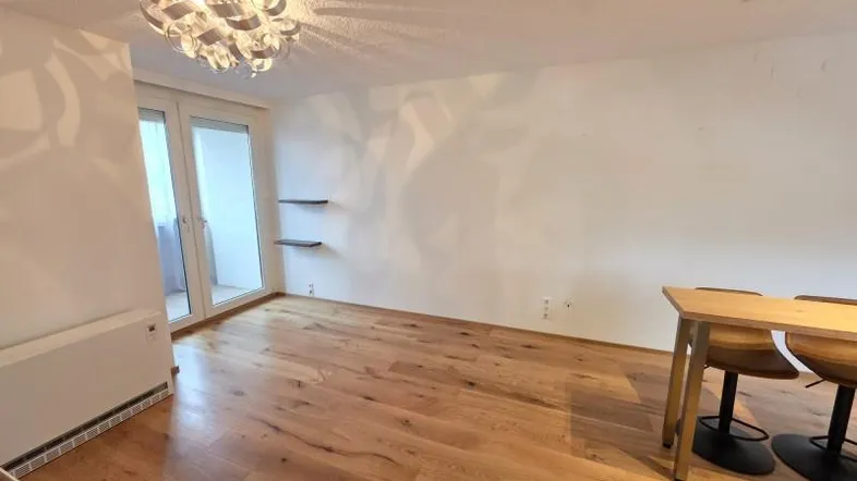 Geräumiger Wohnbereich mit hellem Holzboden, moderner Deckenleuchte und Balkonzugang.