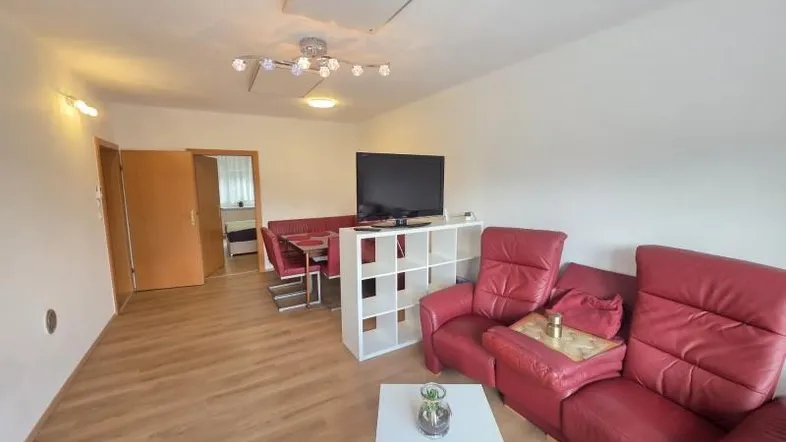 Geräumiger Wohn-Essbereich mit rotem Ledersofa, Esstisch und hellem Laminatboden.