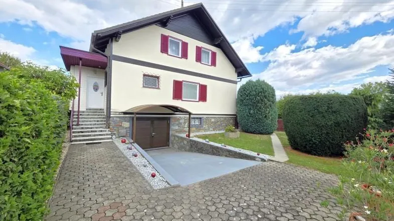 Einfamilienhaus mit gepflasterter Auffahrt und integrierter Garage im Untergeschoss.