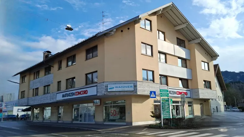 Mehrstöckiges Gebäude an einer Straßenecke mit Geschäften im Erdgeschoss und Wohnungen darüber.