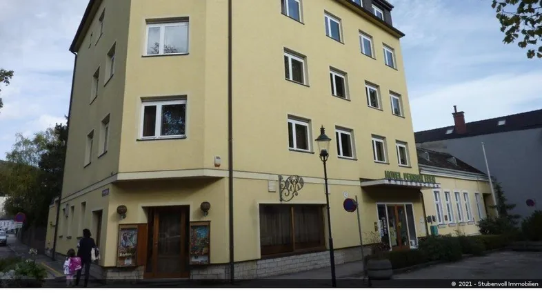 Mehrstöckiges Gebäude mit hellgelber Fassade und mehreren Fenstern unter bewölktem Himmel.