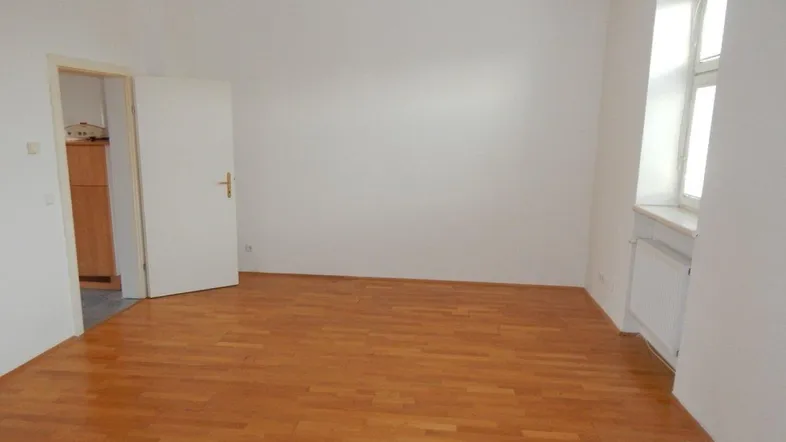 Leeres Zimmer mit warmem Parkettboden und einem Fenster, das den Raum mit natürlichem Licht erfüllt.