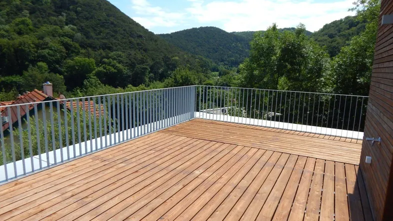 Große Holzterrasse mit modernem Geländer und weitem Blick auf die bewaldeten Hügel.
