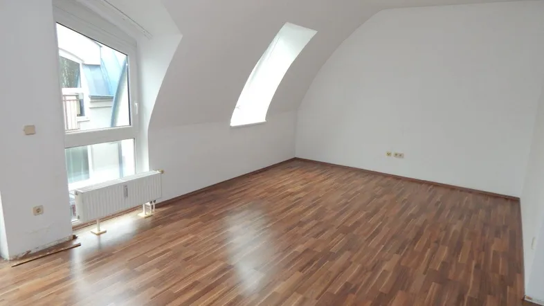 Helles Zimmer mit Dachschrägen, Laminatboden und großem Fenster, bereit zur individuellen Gestaltung.
