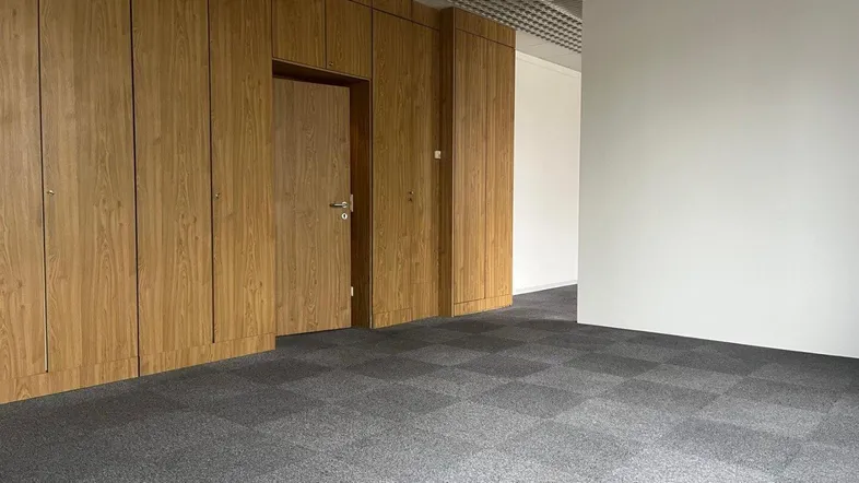 Leerer Büroraum mit eleganter Holzvertäfelung, integrierter Tür, modernem Teppichboden und abgehängter Decke.