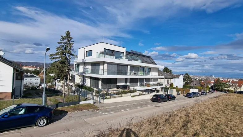 Modernes Mehrfamilienhaus mit mehreren Balkonen und Blick auf die Stadt.