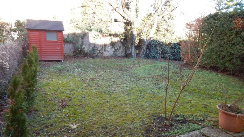 Gepflegter Garten mit Rasenfläche, Bäumen und einem kleinen Geräteschuppen.