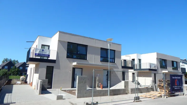Moderne Doppelhaushälfte im Bau mit klaren Linien und Balkonen unter blauem Himmel.