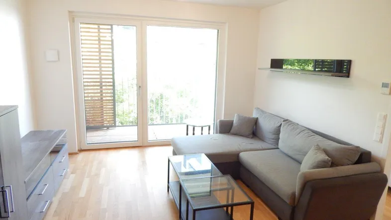 Helles Wohnzimmer mit modernem Sofa, Holzboden und Zugang zum Balkon.